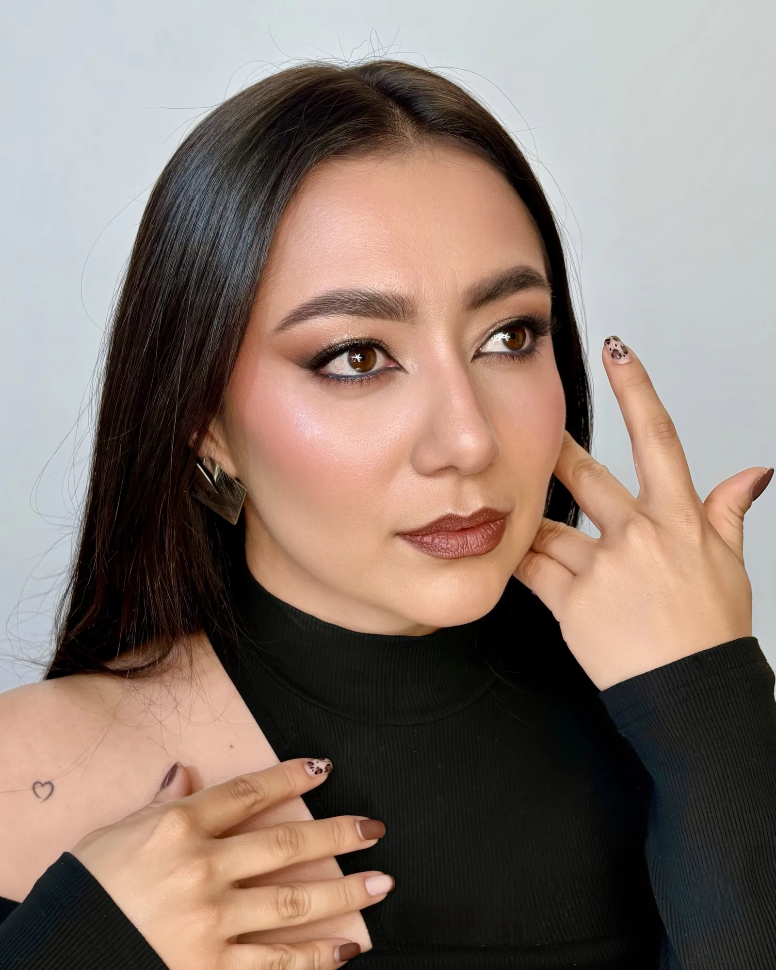 Maquillaje social con ojos definidos en tonos marrones, piel luminosa y labial marrón rojizo, con cuello alto negro