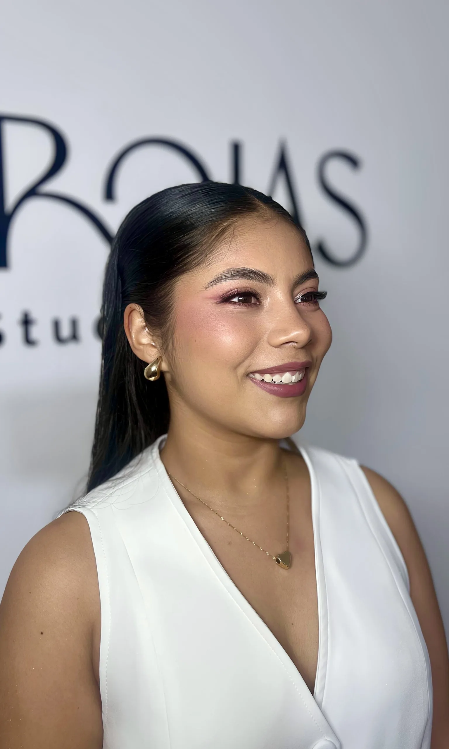 Retrato de una mujer sonriente con maquillaje de ojos rosado y blusa blanca.