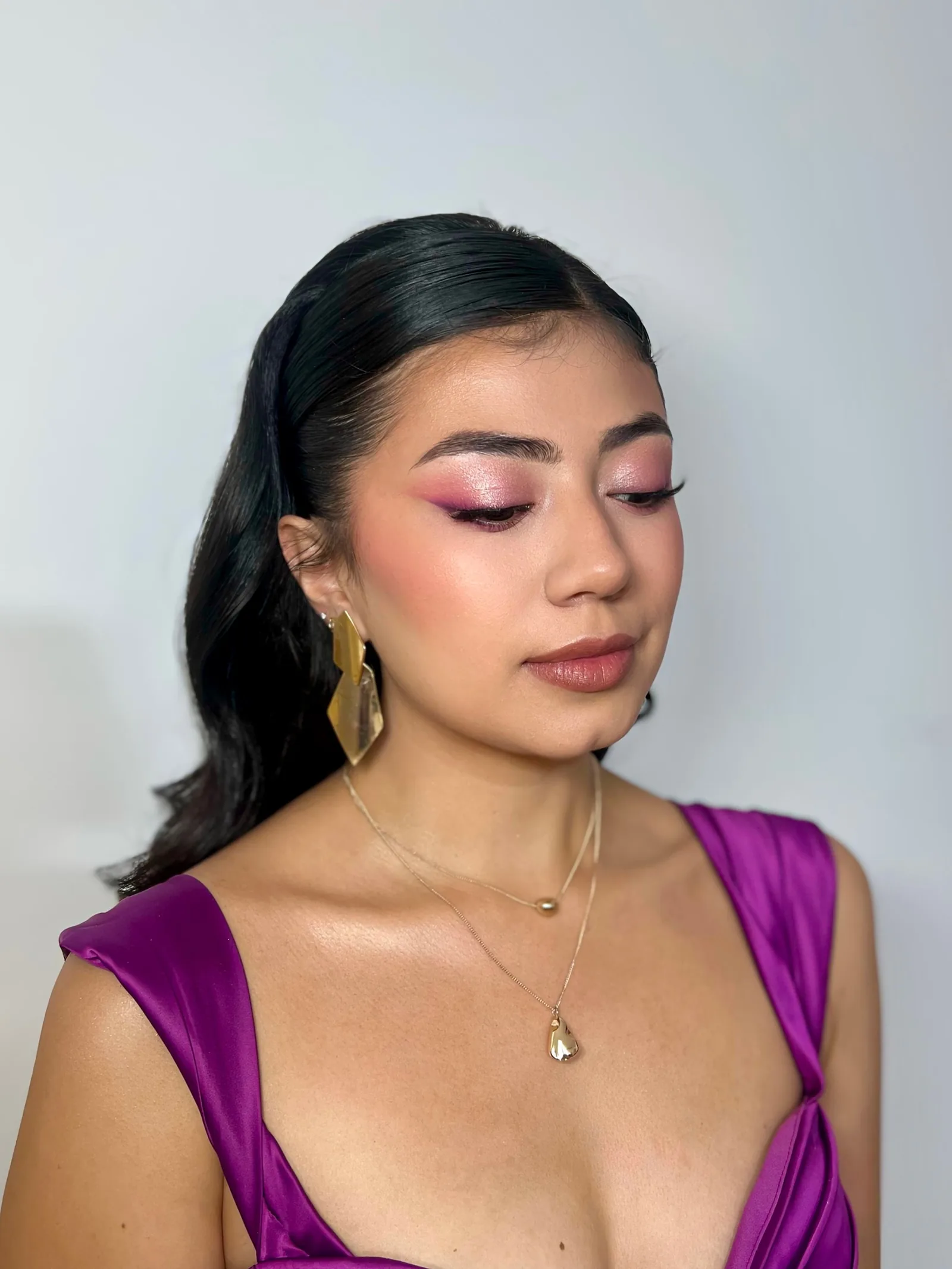 Maquillaje social con sombra rosa, delineado gráfico, rubor melocotón y labial nude rosado, con vestido satinado morado