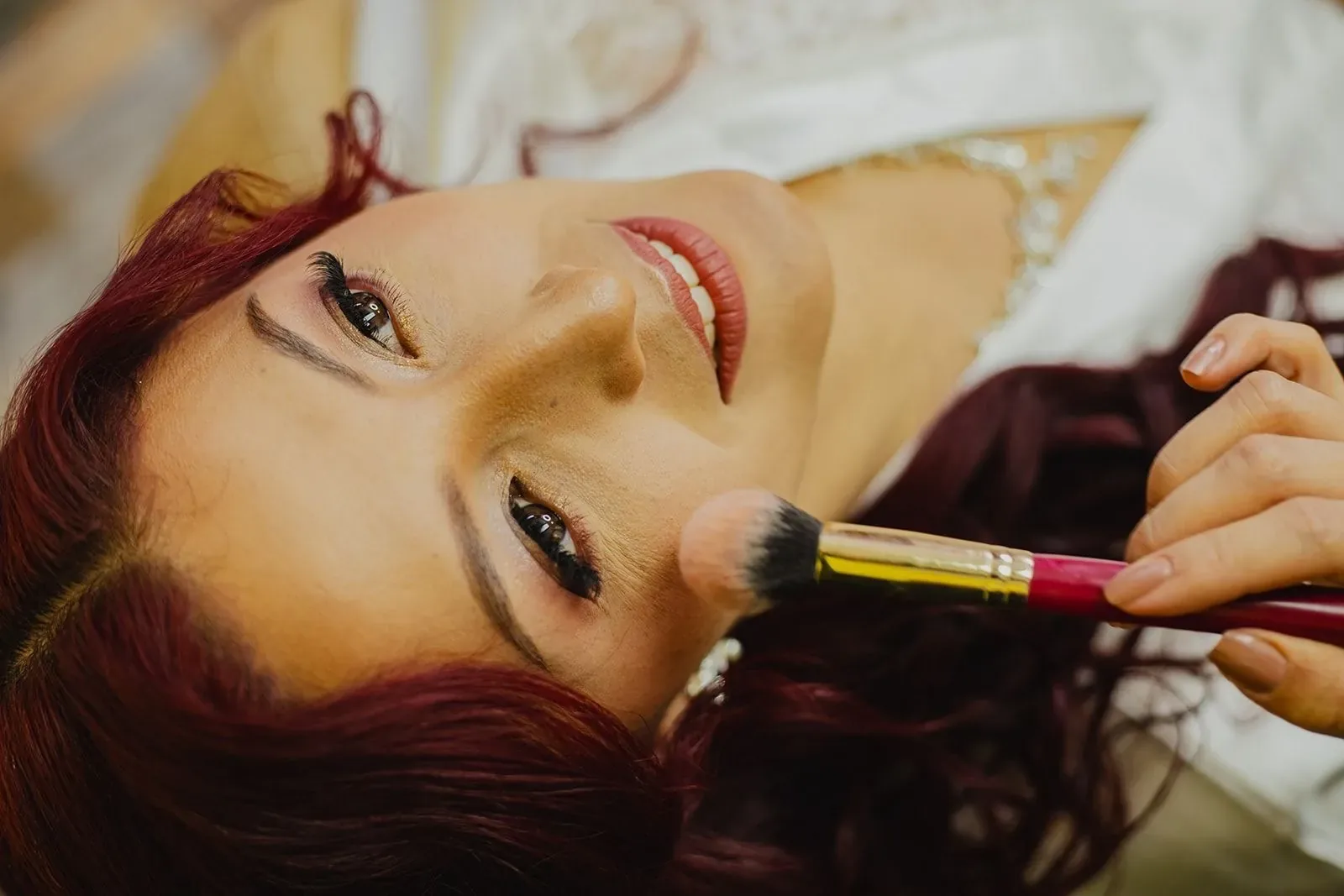Detalle del maquillaje de novia de Andre: pestañas, sombra dorada y labios coral, con brocha de rubor