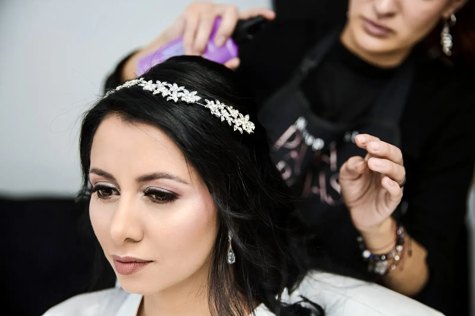 Caro con maquillaje de novia de ojos ahumados y labios nude mientras le fijan el peinado con tiara