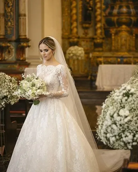 Novia con vestido de encaje y velo, sosteniendo un ramo en una iglesia.