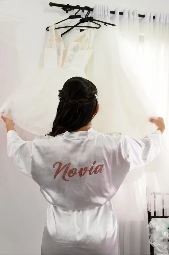 Erika de espaldas en bata de novia, con peinado semirrecogido trenzado, sostiene su vestido de tul colgado