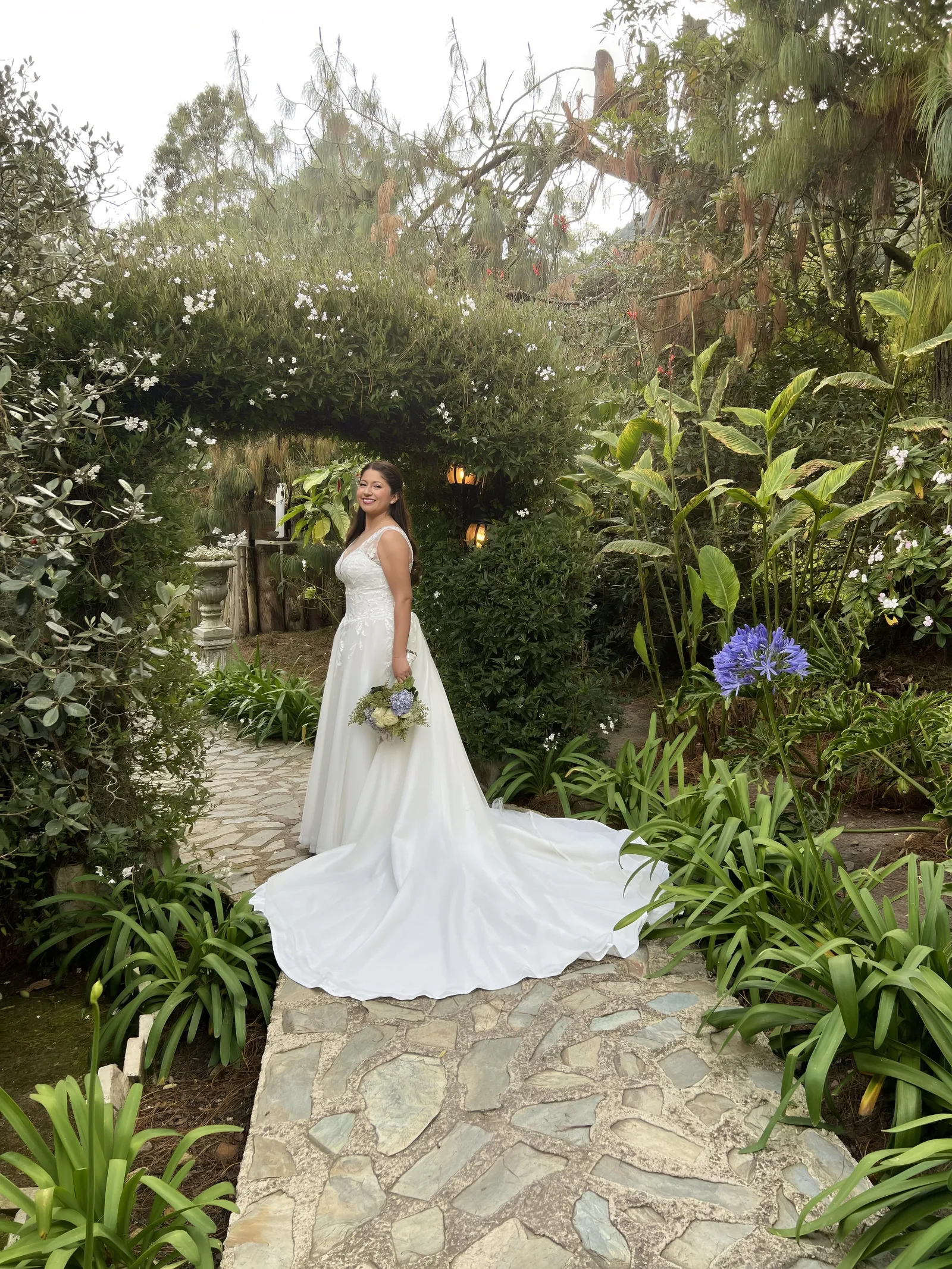 Bride in a white gown holding a bouquet in a leafy garden.