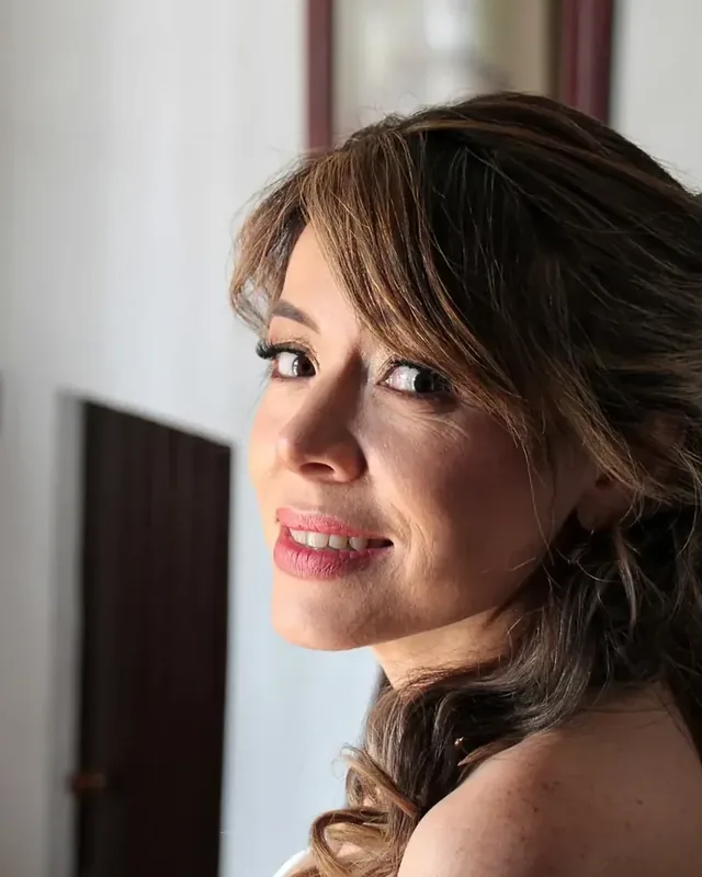 Ginita mira sobre el hombro con maquillaje de novia de labios rosados y semirrecogido con flequillo