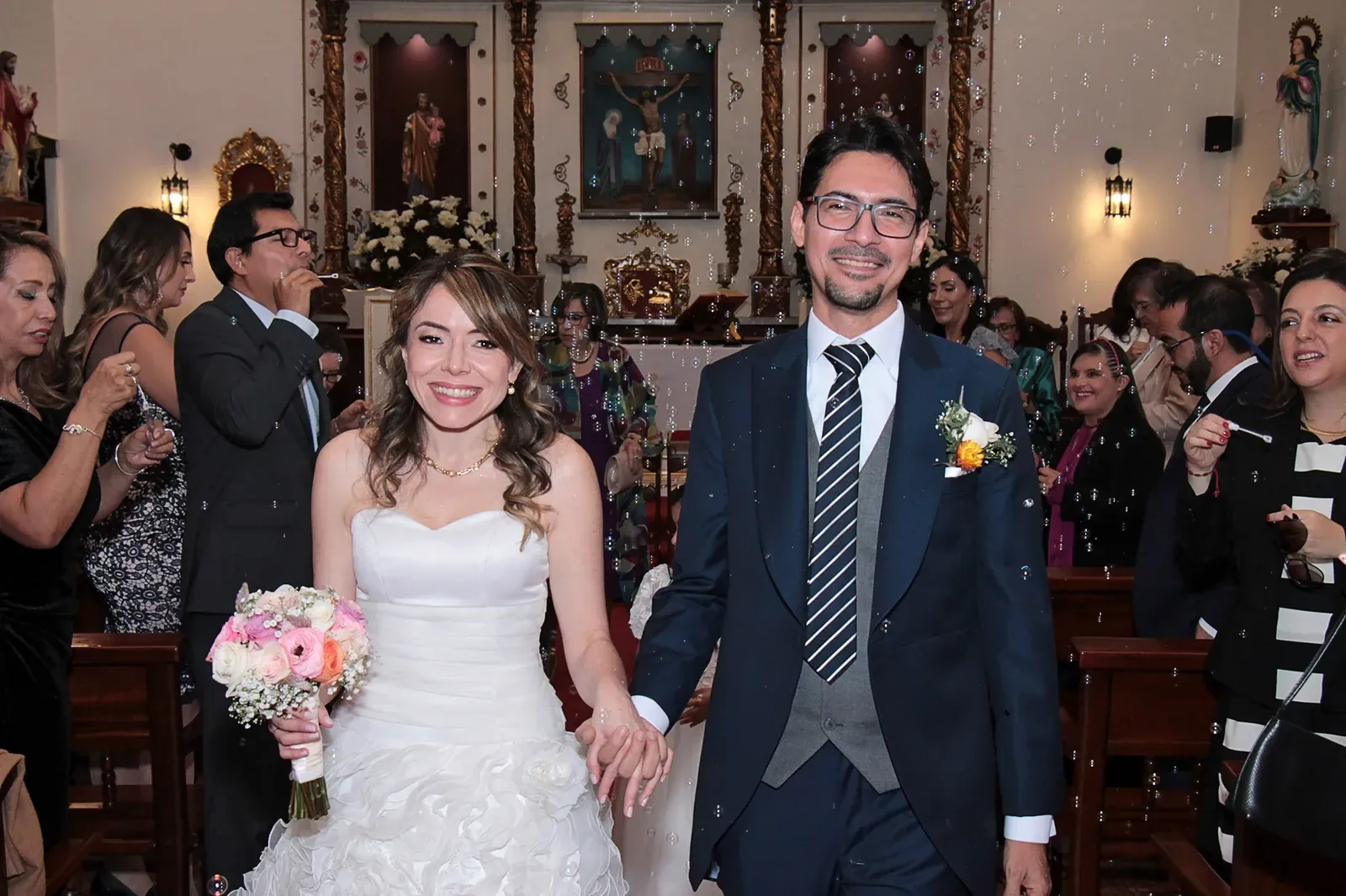 Ginita sale de la capilla tomada de la mano del novio, con maquillaje de novia luminoso y ramo de rosas