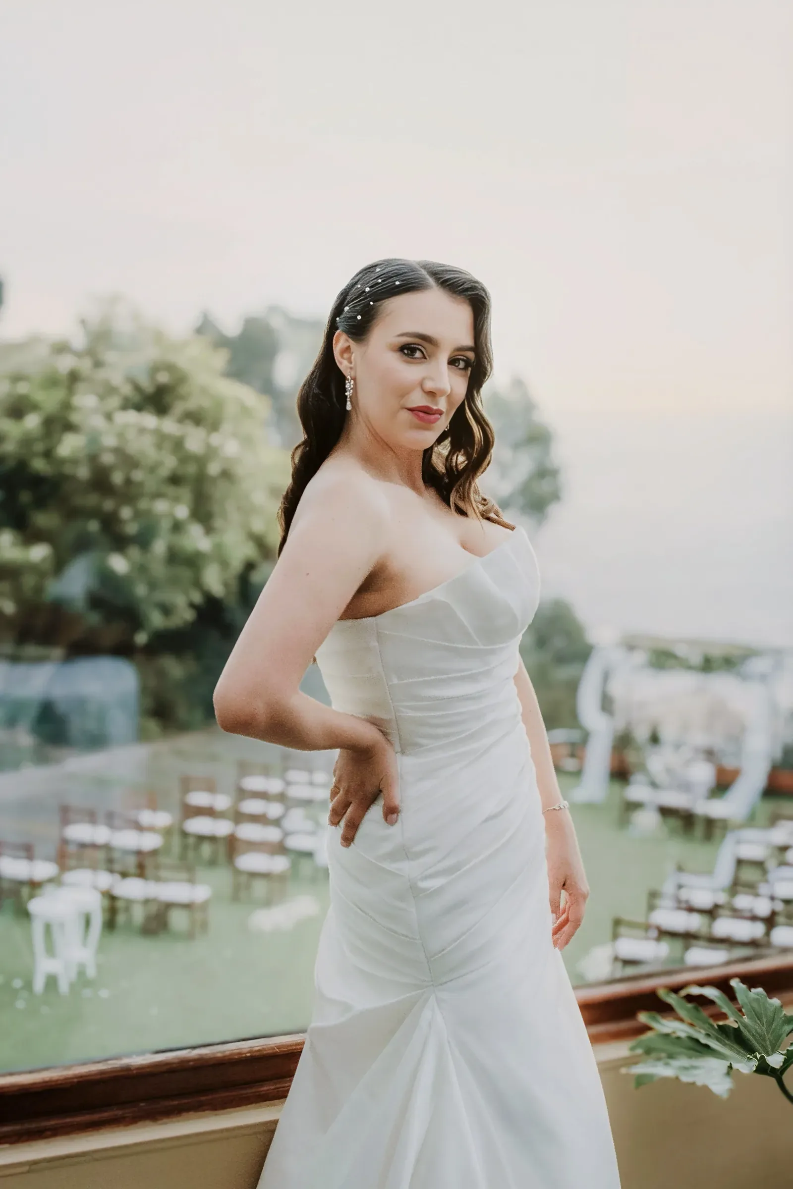 Katha con maquillaje de novia de labios rojos, mano en la cintura y vestido strapless drapeado