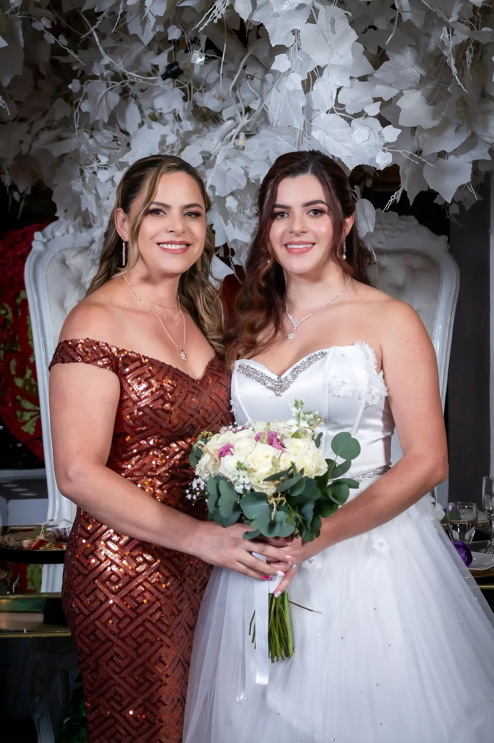 Kelly con maquillaje de novia de piel luminosa y escote corazón con pedrería, junto a una invitada