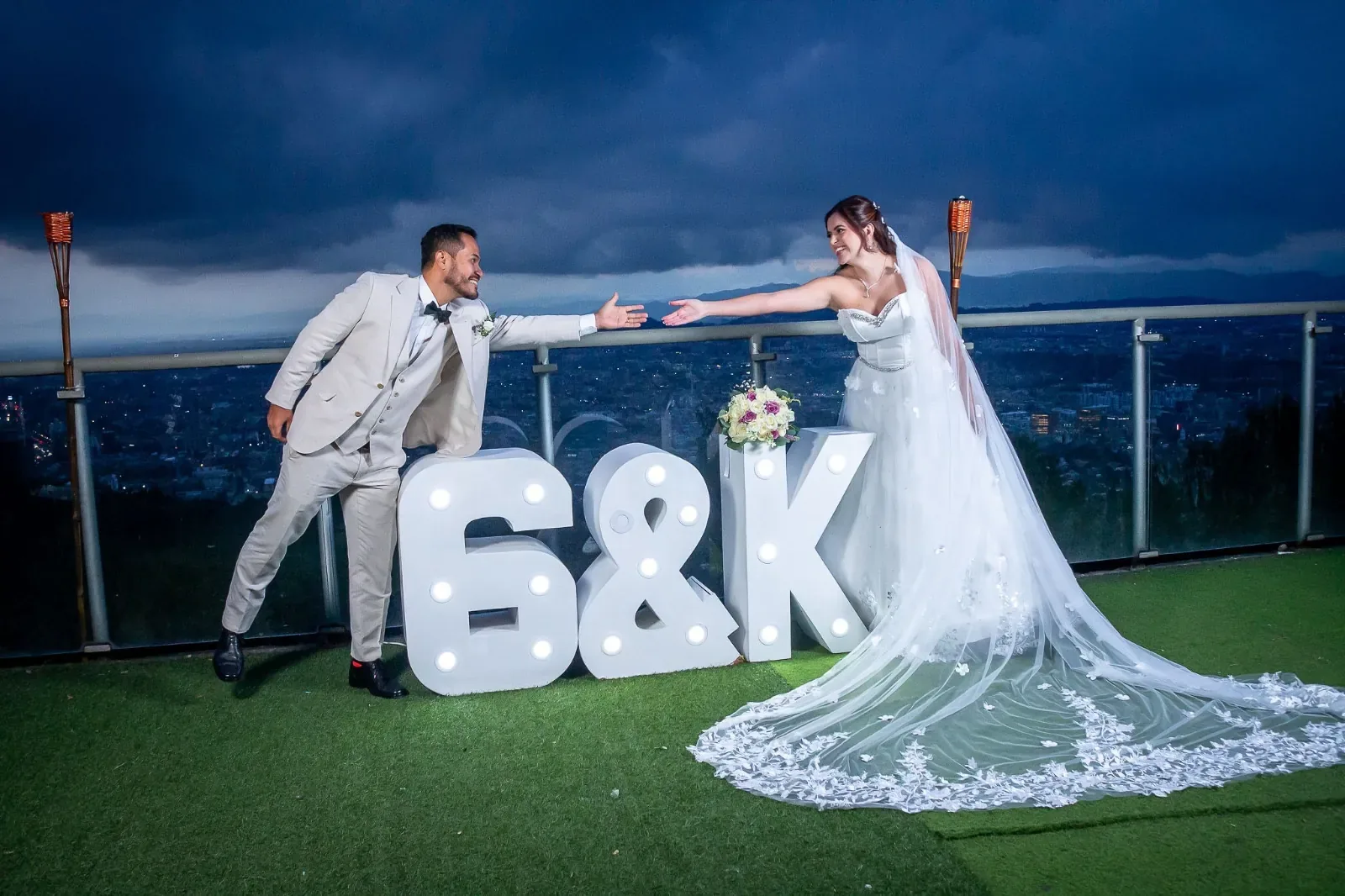 Kelly con maquillaje de novia y velo largo de encaje extiende la mano al novio en una terraza al atardecer