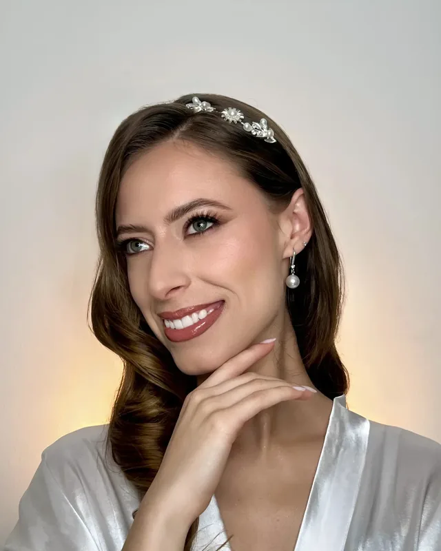 Lau sonríe con maquillaje de novia de labios rosa brillante, tiara de perlas y ondas hacia un lado