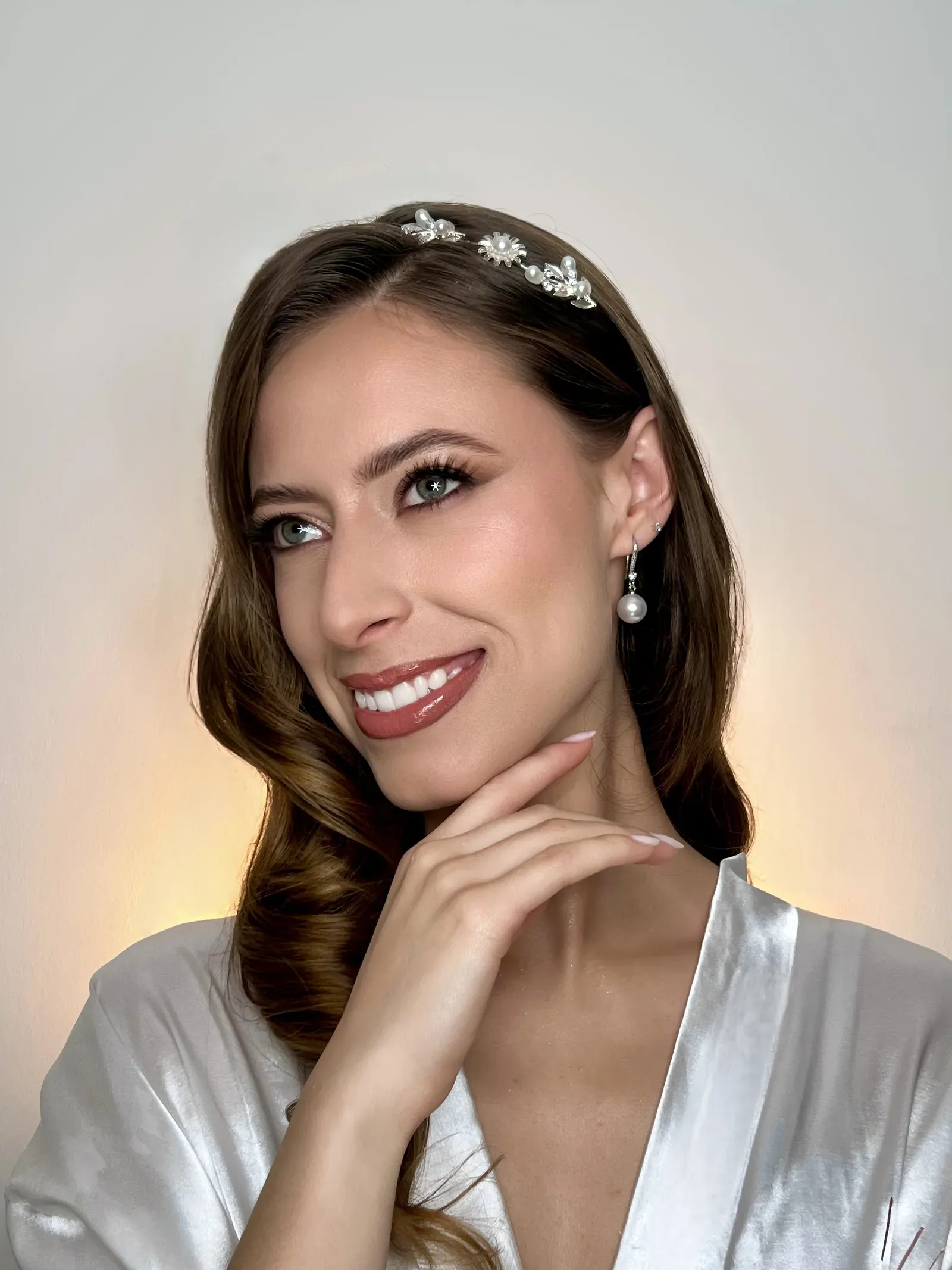 Lau sonríe con maquillaje de novia de labios rosa brillante, tiara de perlas y ondas hacia un lado