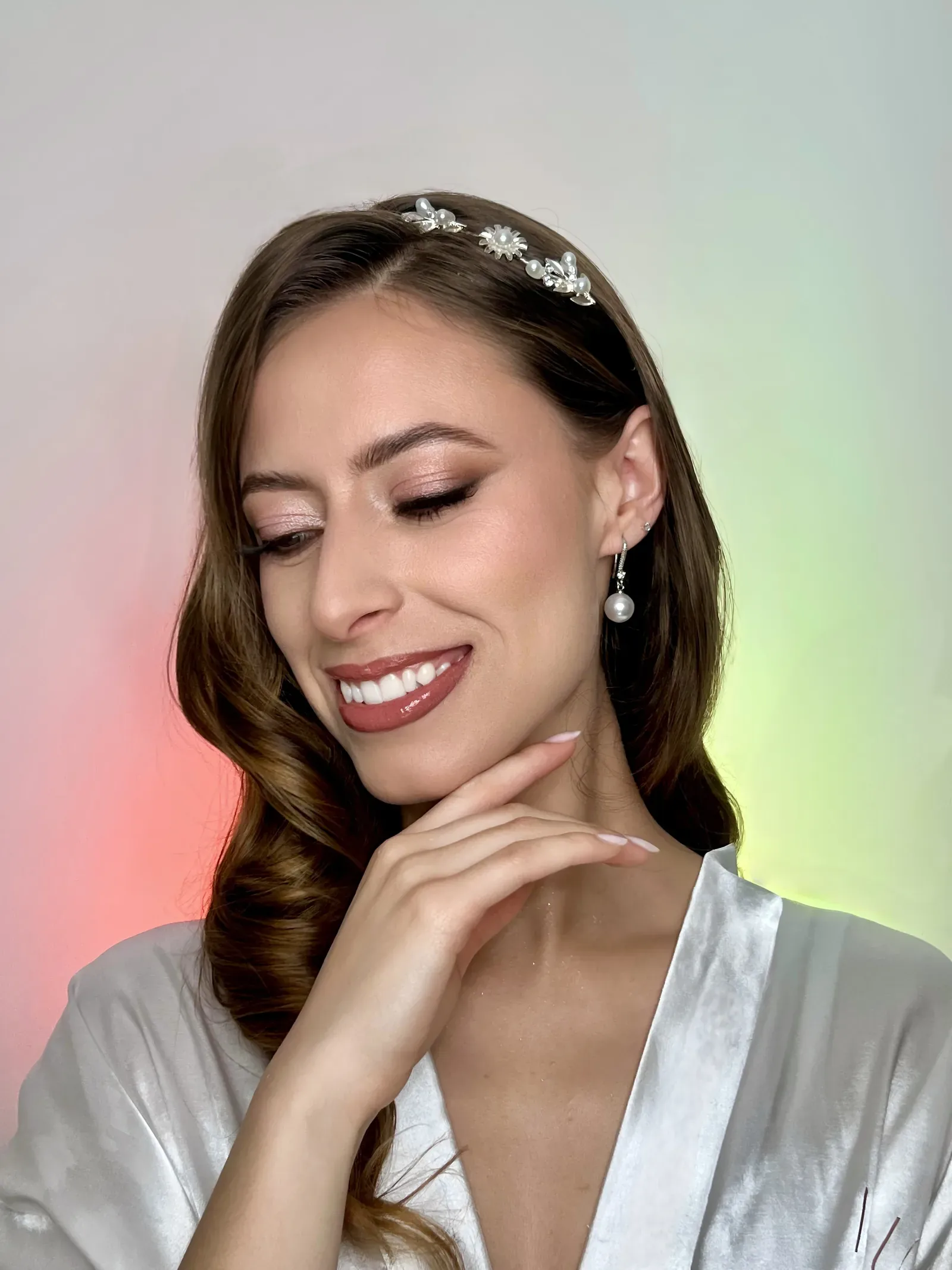 Lau sonríe mirando hacia abajo con maquillaje de novia de sombra rosada, aretes de perla y tiara floral