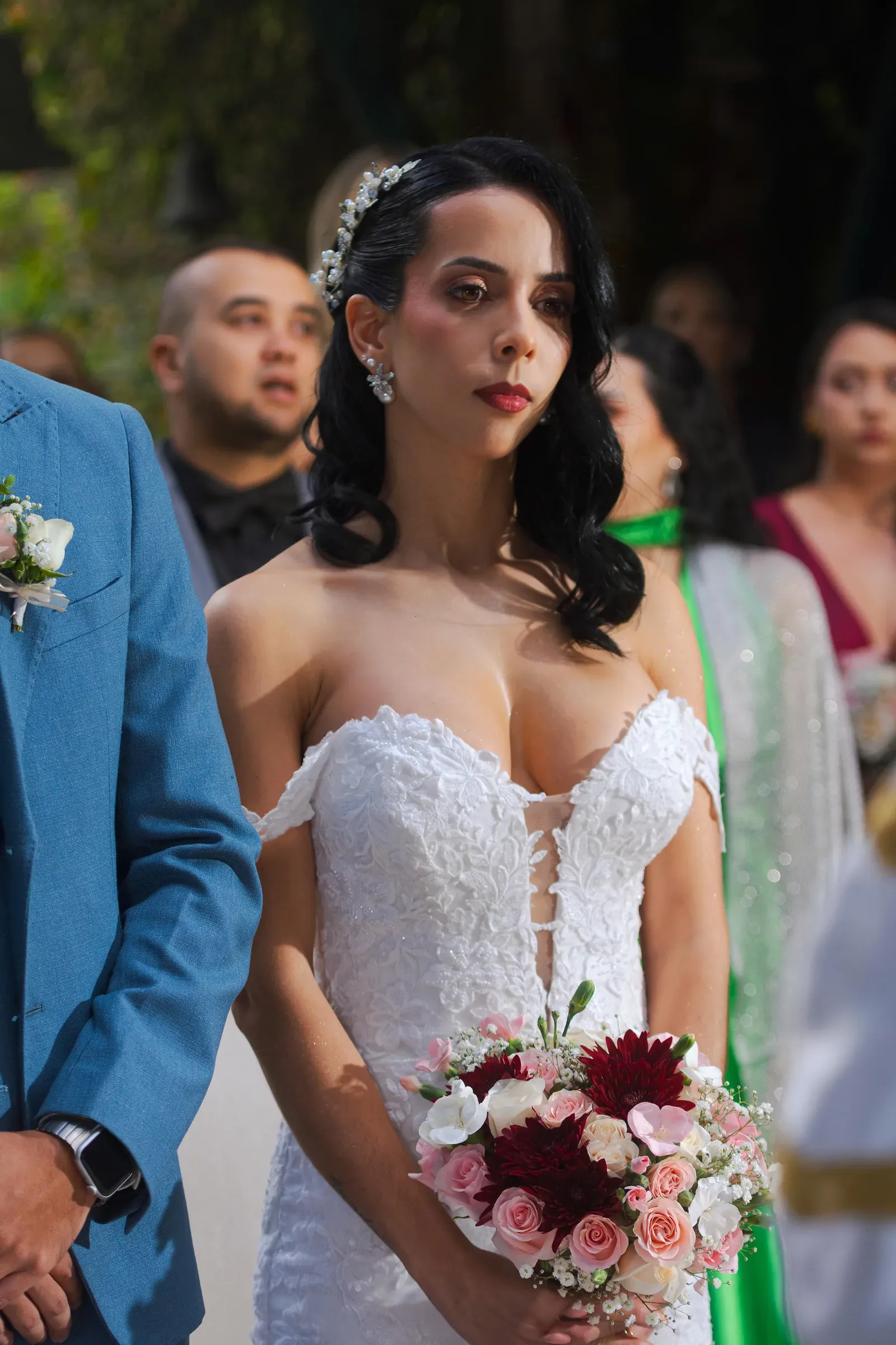 Laura de pie en la ceremonia con maquillaje de novia de labios rojos, vestido de encaje y ramo rosa y vino