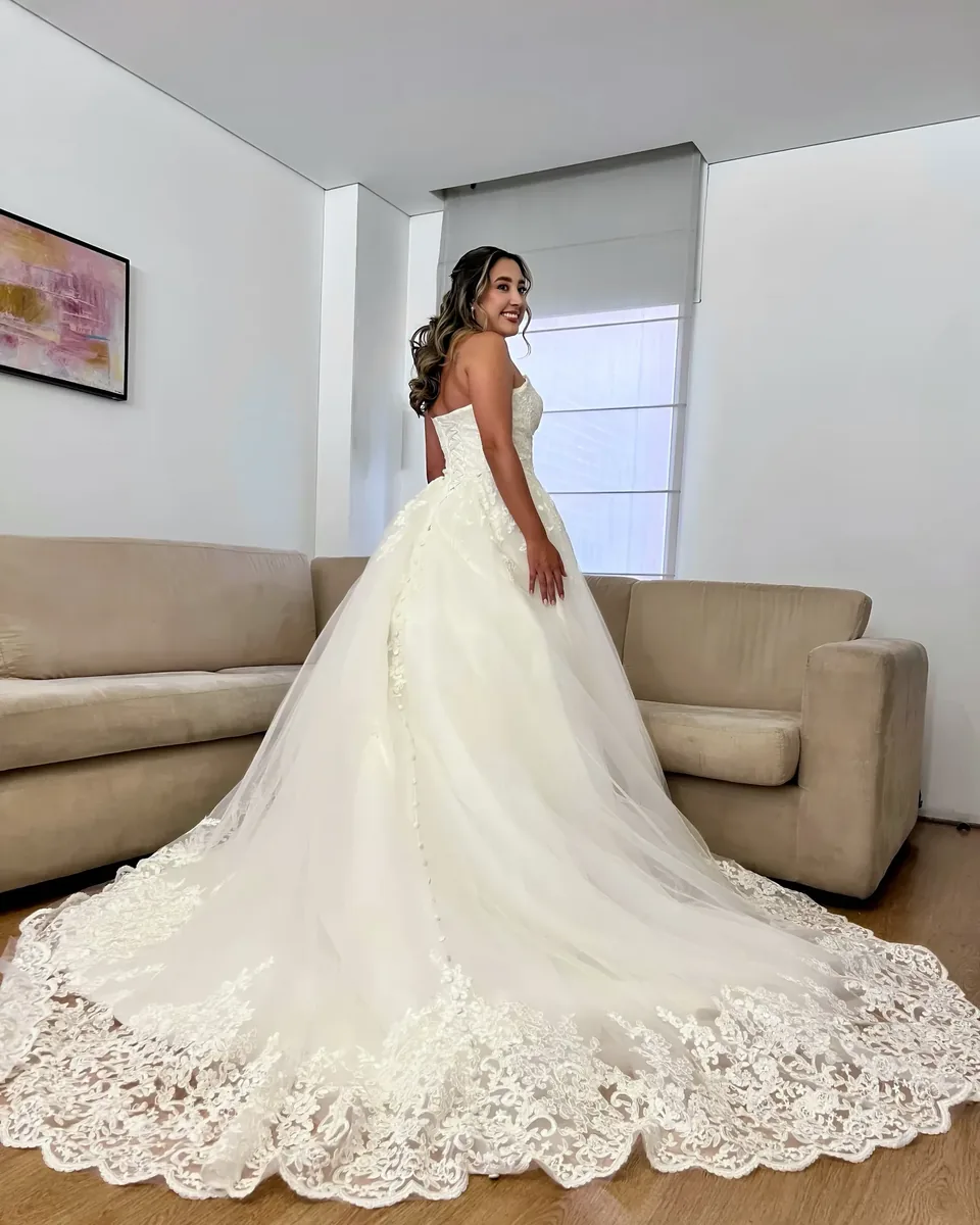 Laura mira atrás con maquillaje de novia, semirrecogido en ondas y vestido strapless de encaje con cola