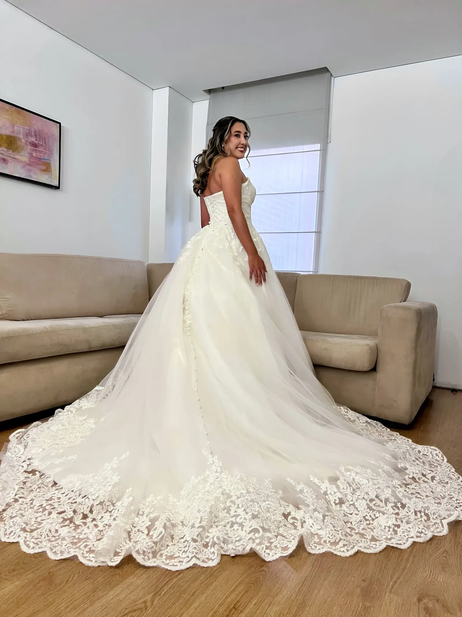Laura mira atrás con maquillaje de novia, semirrecogido en ondas y vestido strapless de encaje con cola