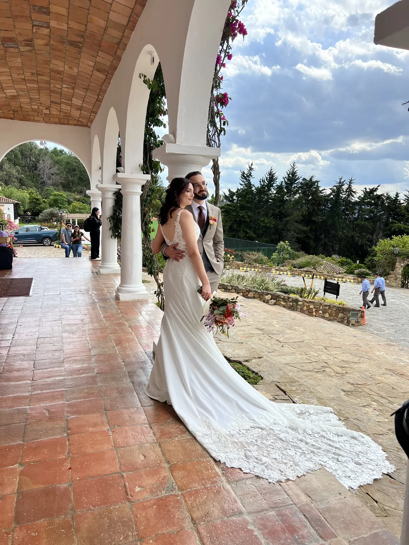 Laura con maquillaje de novia y ondas sueltas posa abrazada con el novio bajo arcos blancos