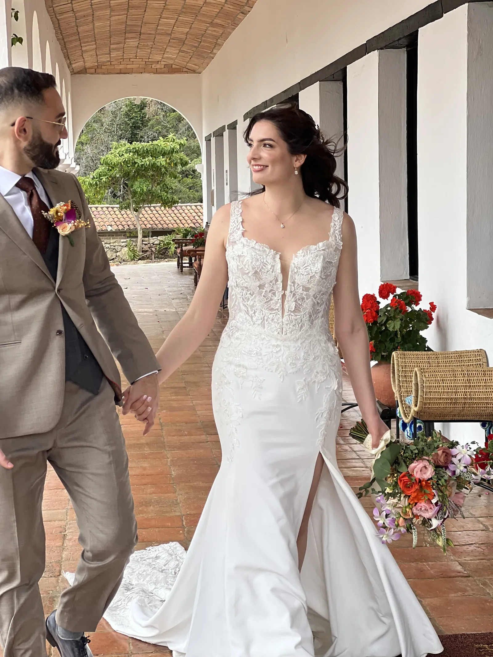 Laura con maquillaje de novia natural y recogido suelto camina de la mano del novio por un corredor