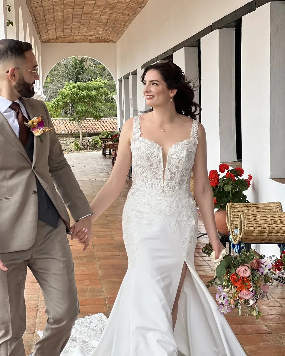 Laura con maquillaje de novia natural y recogido suelto camina de la mano del novio por un corredor