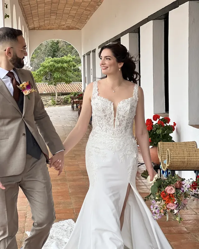 Laura con maquillaje de novia natural y recogido suelto camina de la mano del novio por un corredor
