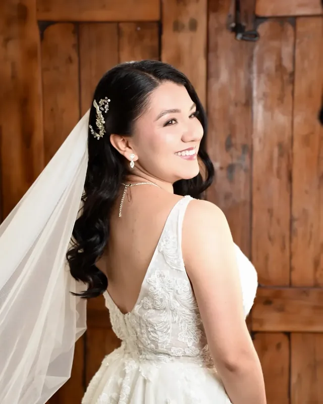 Luisa mira sobre el hombro con maquillaje de novia luminoso, ondas largas, tocado de cristales y velo