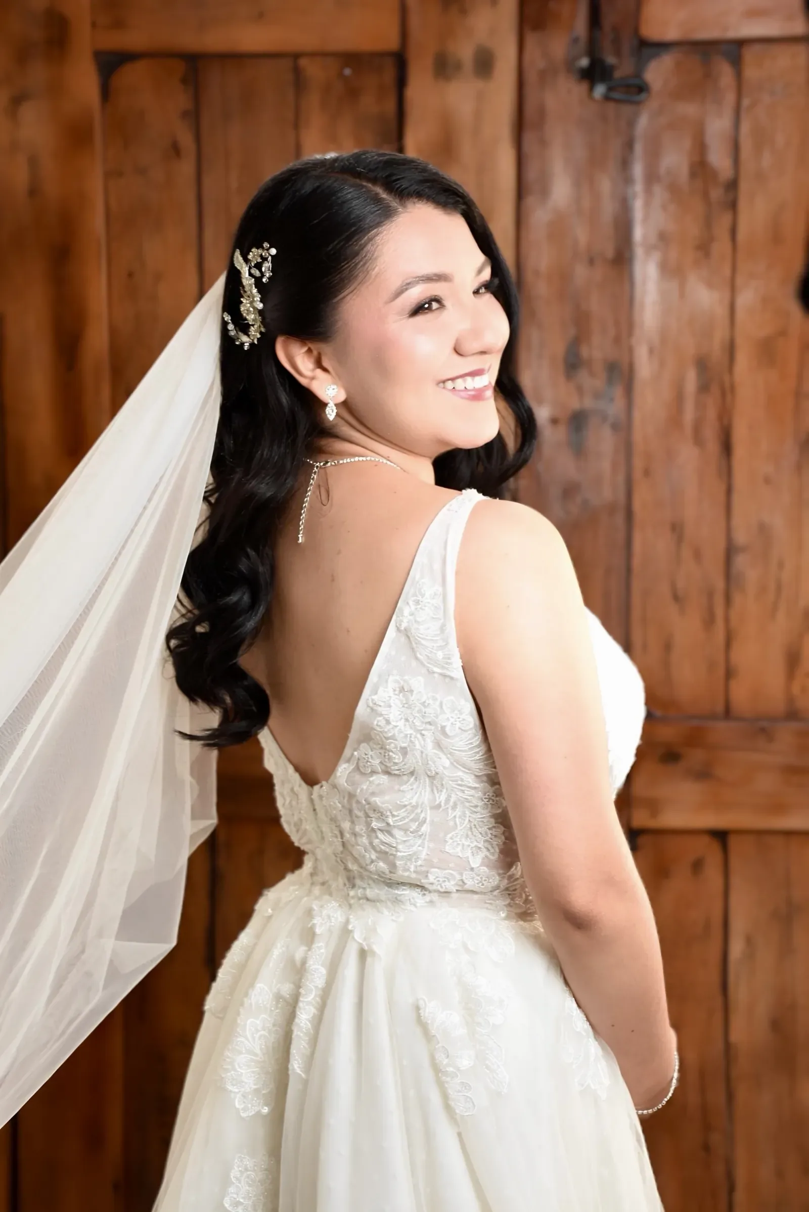Luisa mira sobre el hombro con maquillaje de novia luminoso, ondas largas, tocado de cristales y velo