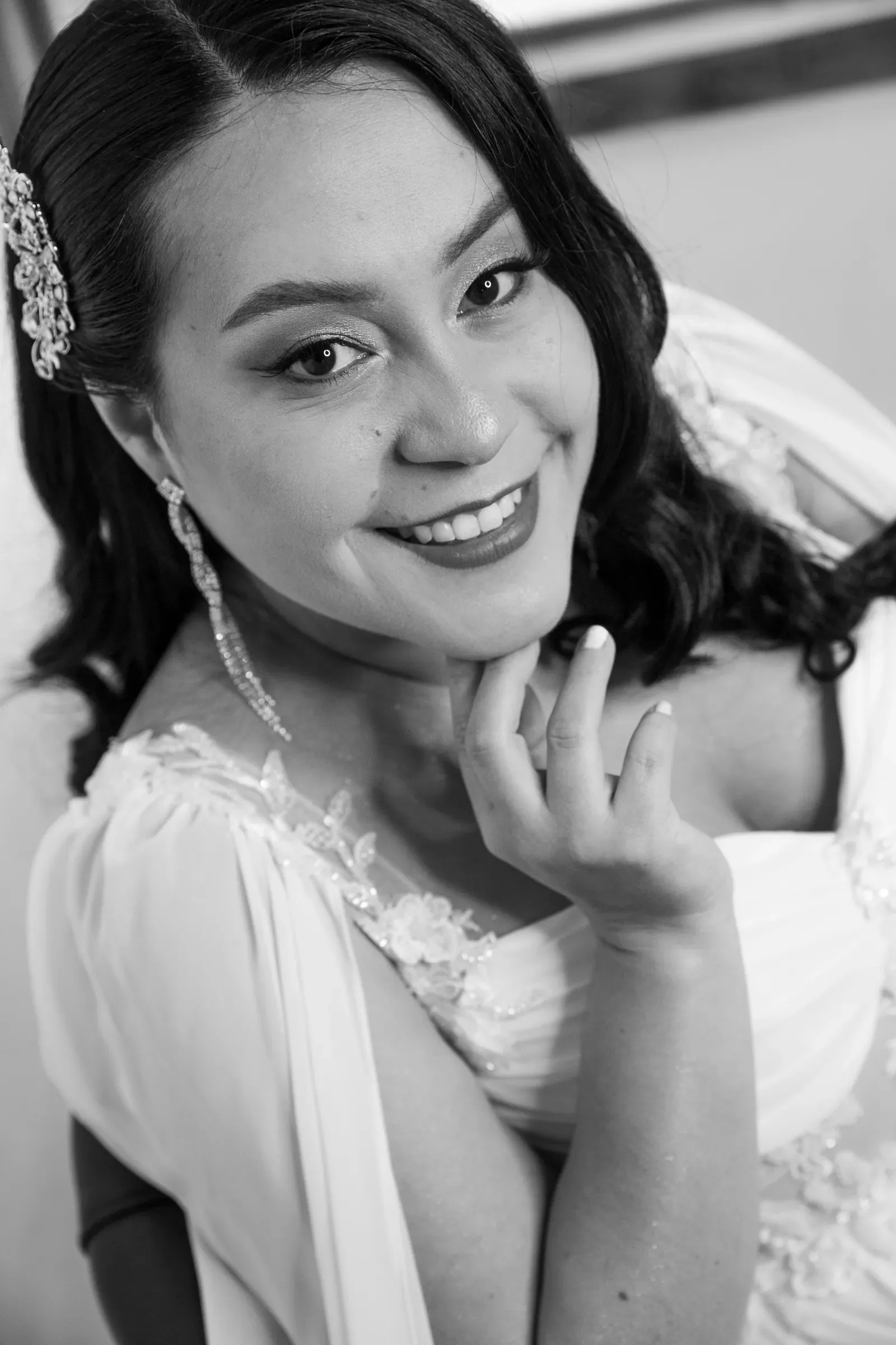 Luisa sonríe con maquillaje de novia luminoso, ondas suaves y tocado de cristales, en blanco y negro