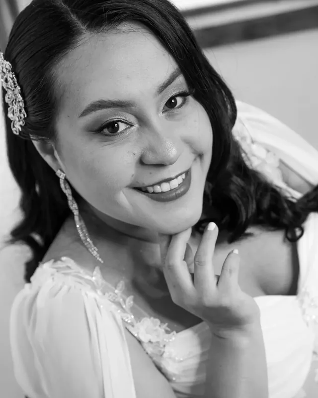 Luisa sonríe con maquillaje de novia luminoso, ondas suaves y tocado de cristales, en blanco y negro