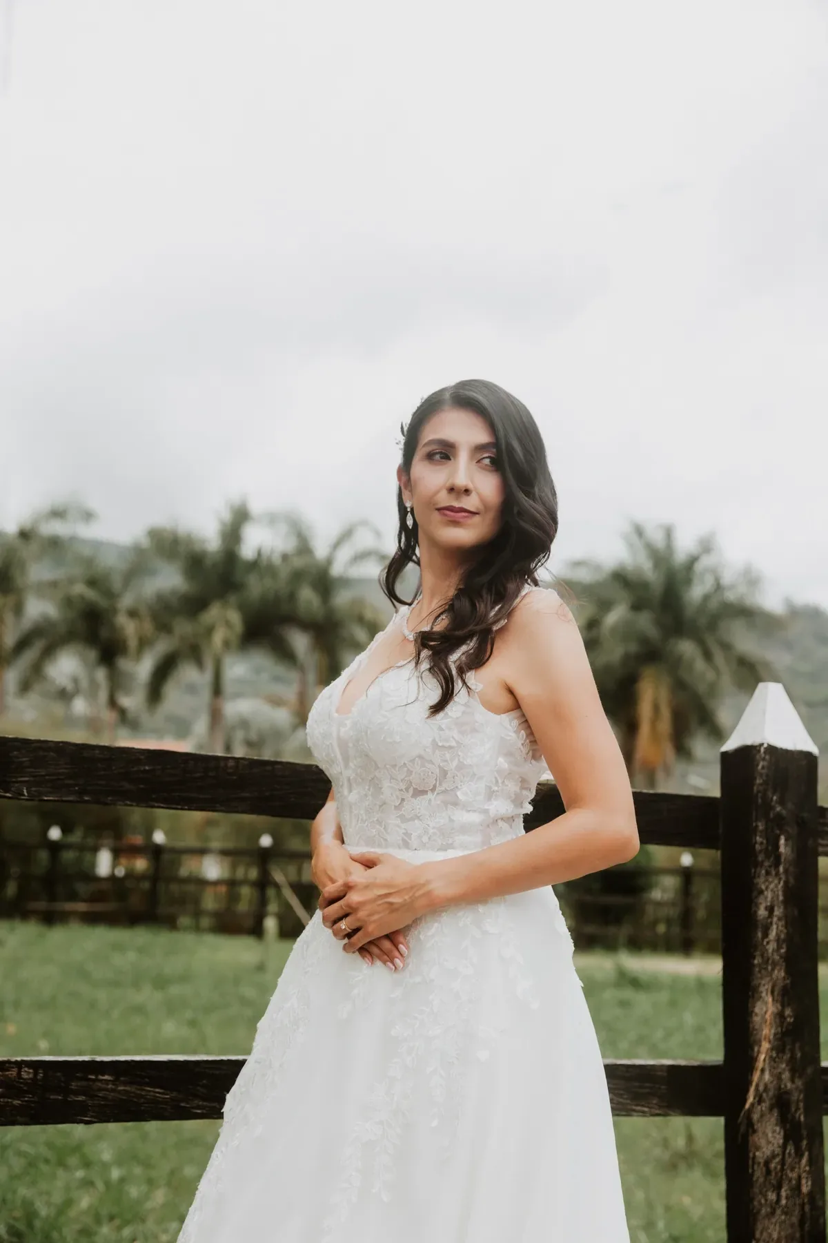 Luisa con maquillaje de novia y labios vino, ondas a un lado, junto a una cerca de madera en el campo