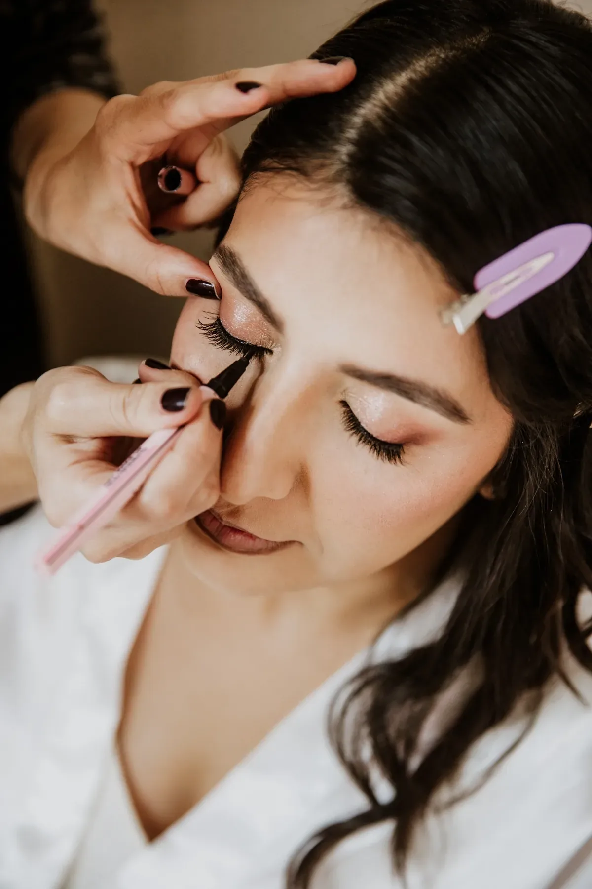 Luisa con ojos cerrados mientras le delinean el ojo para su maquillaje de novia con sombra dorada