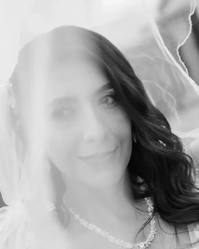 Luisa sonríe bajo el velo con maquillaje de novia suave, ondas sueltas y collar de cristales