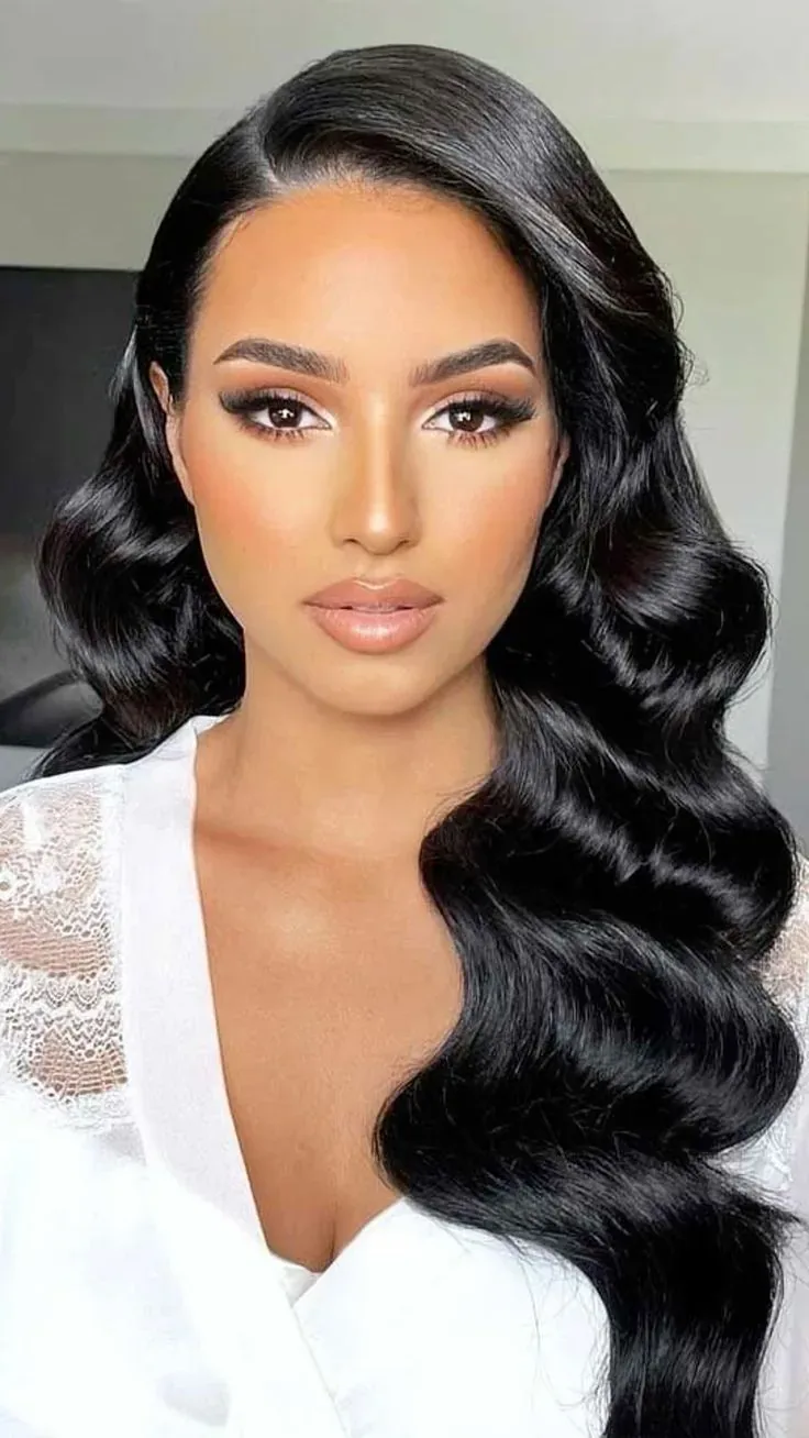 Mujer con maquillaje glamuroso, cabello negro ondulado y prenda blanca de encaje.