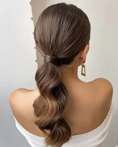 Bridal hairstyle with a low wavy ponytail and a white off-the-shoulder dress.