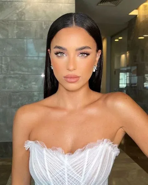 Portrait of a bride with sleek dark hair, defined makeup, and a strapless white dress.