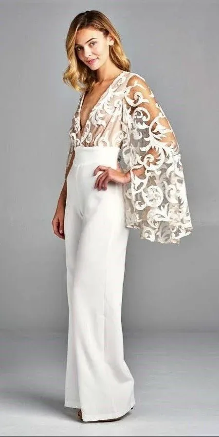 Woman wearing a white wedding dress with an embroidered lace cape in a studio.