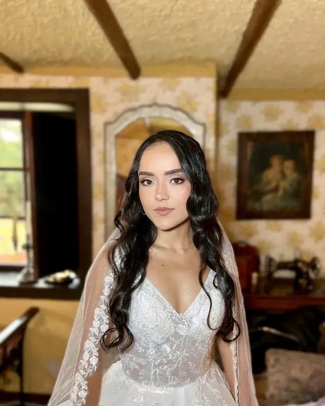 Natalie con maquillaje de novia de piel luminosa, ojos en tonos rosados y ondas largas bajo un velo de encaje