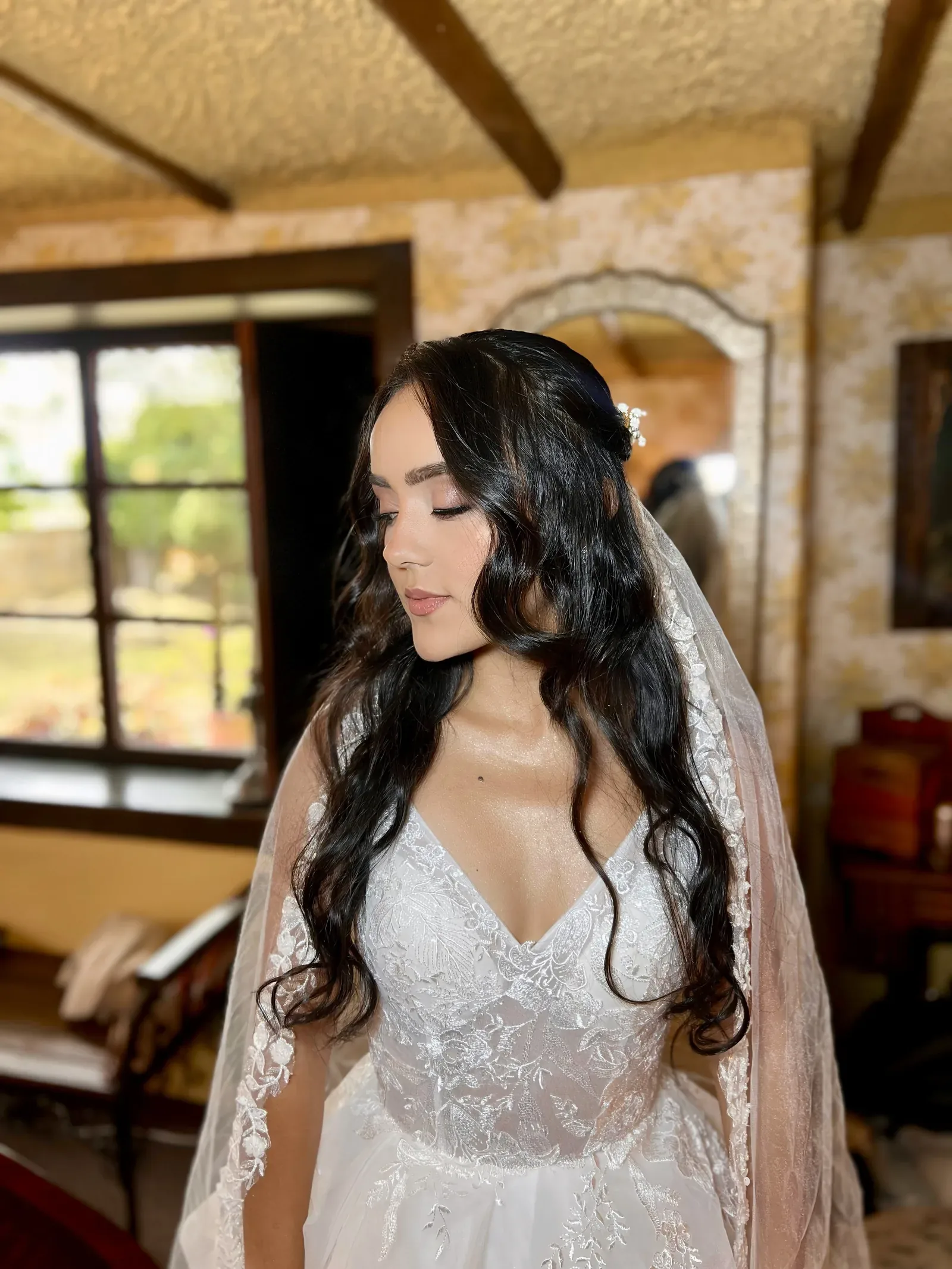 Natalie de perfil con maquillaje de novia suave, ondas largas y un pequeño tocado de perlas sujetando el velo
