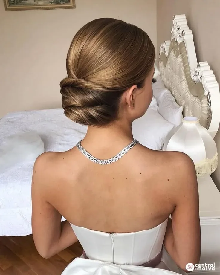 Novia vista de espaldas con recogido bajo, collar de brillantes y vestido blanco sin tirantes.