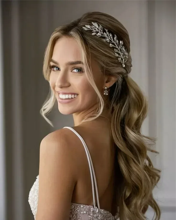 Novia sonriente con ondas largas, tocado plateado y vestido de encaje.