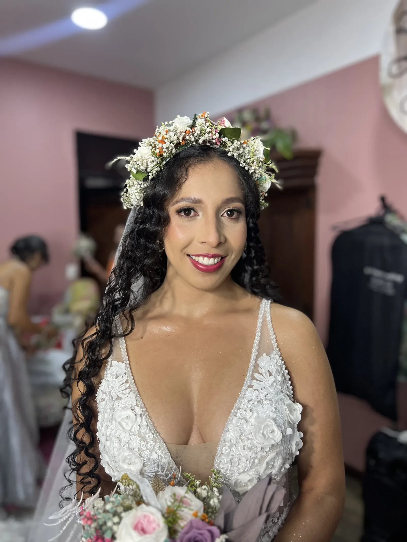 Stefa sonríe de frente con maquillaje de novia de piel luminosa, labios fucsia y corona de flores
