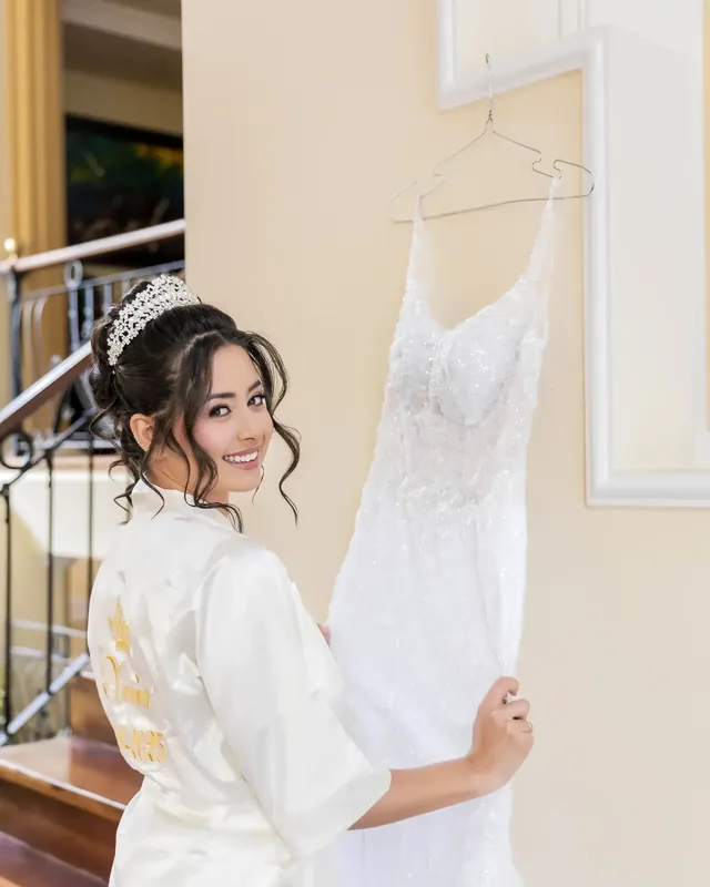 Tatiana smiles in bridal makeup, tiara and updo, wearing an embroidered robe beside her gown