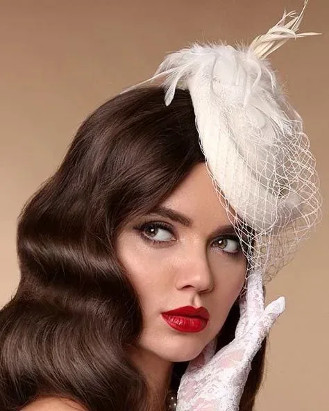 Retrato de novia con ondas vintage, labios rojos y tocado blanco con velo de red.